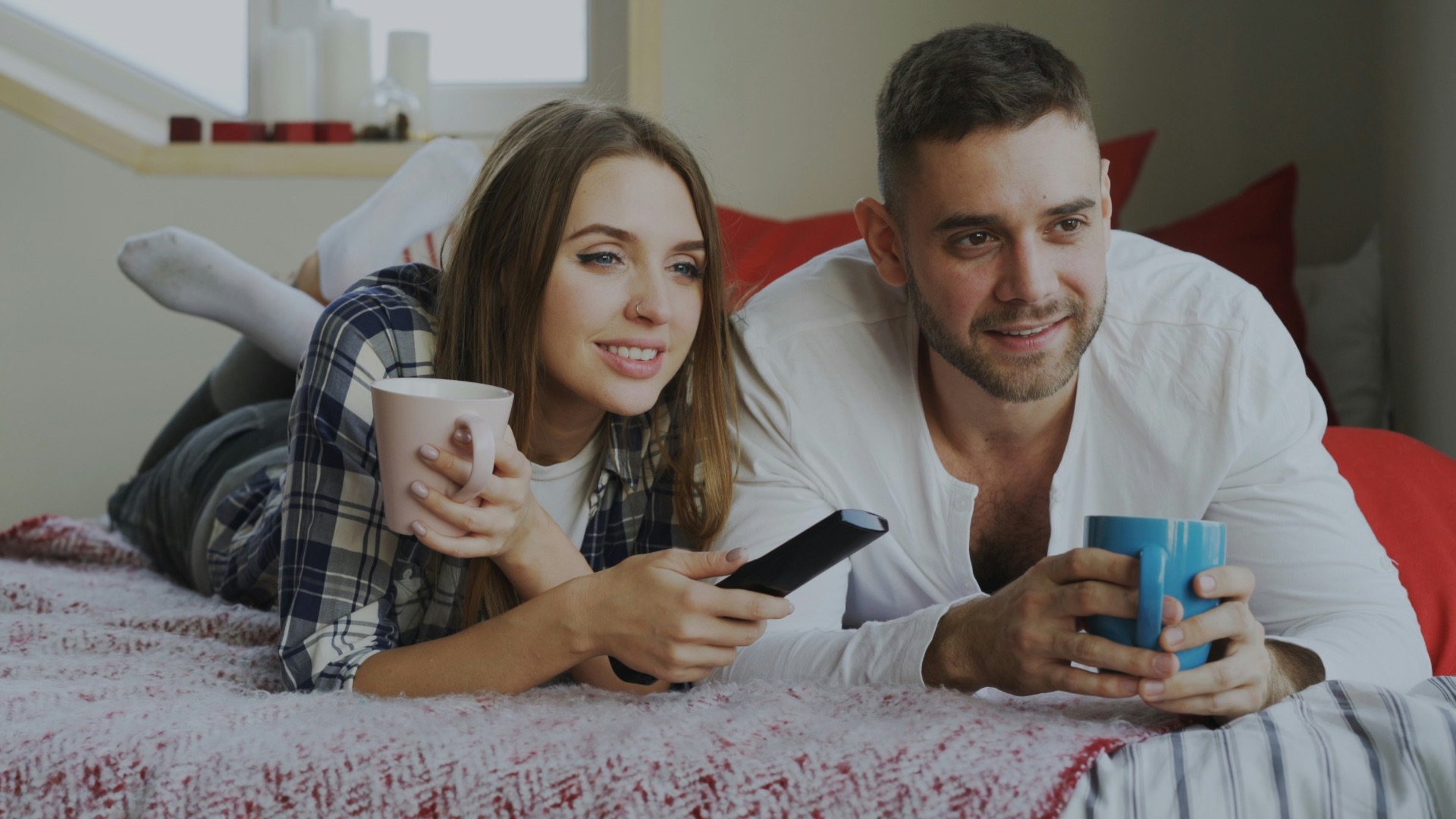 Couple relaxing on bed with coffee and remote.
