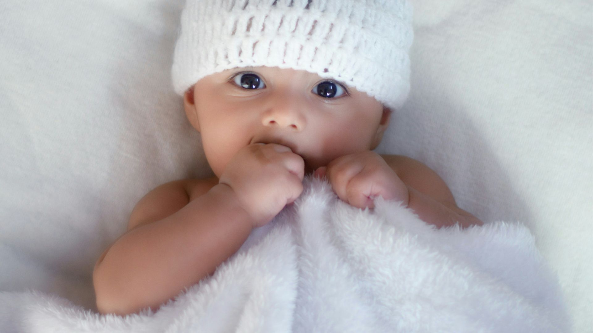 baby in white knit cap lying on white textile