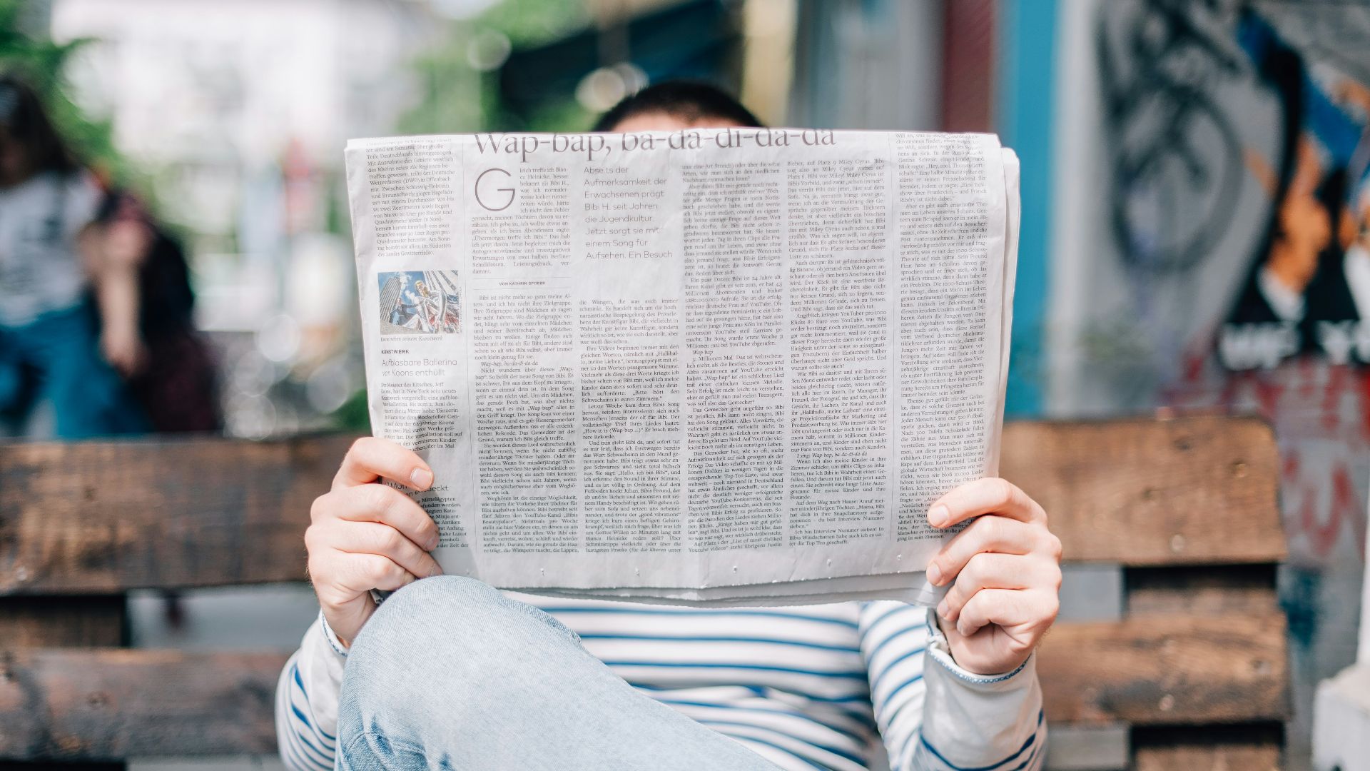 man sitting on bench reading newspaper