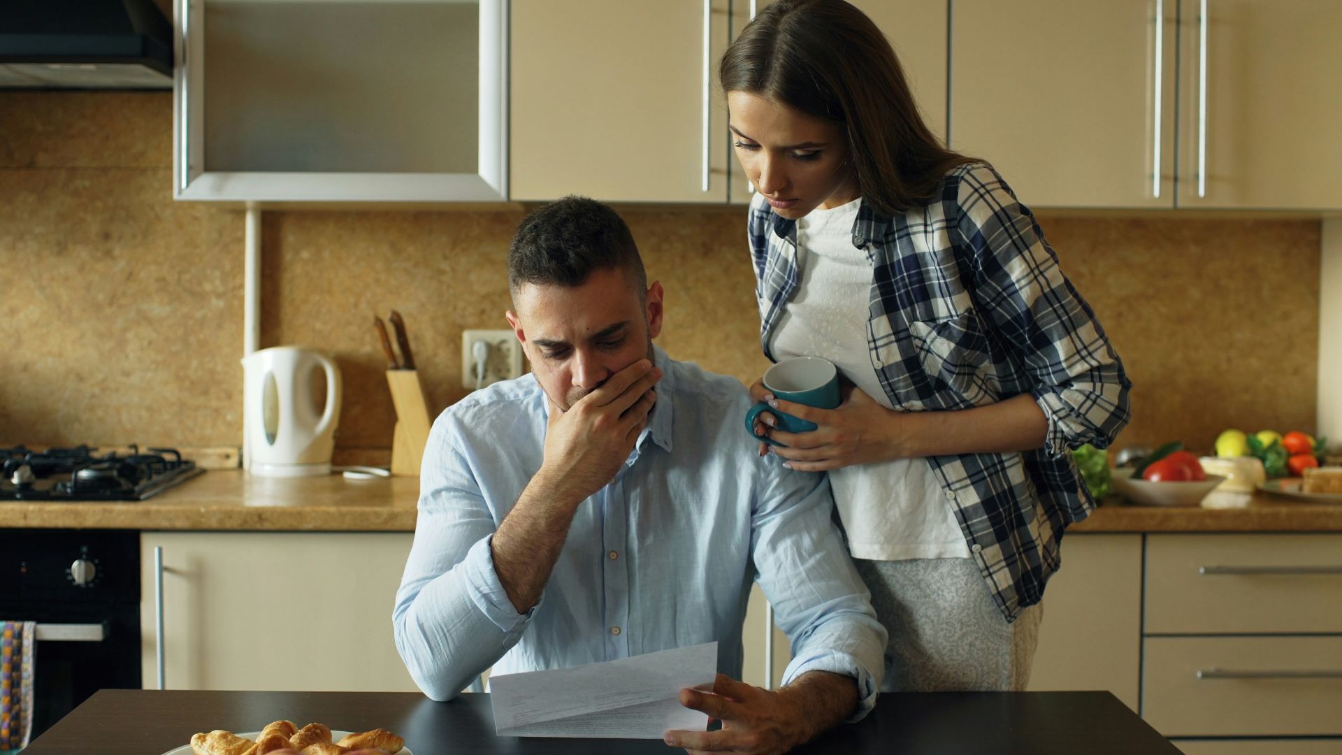 Couple looking stressed over bills at kitchen table.