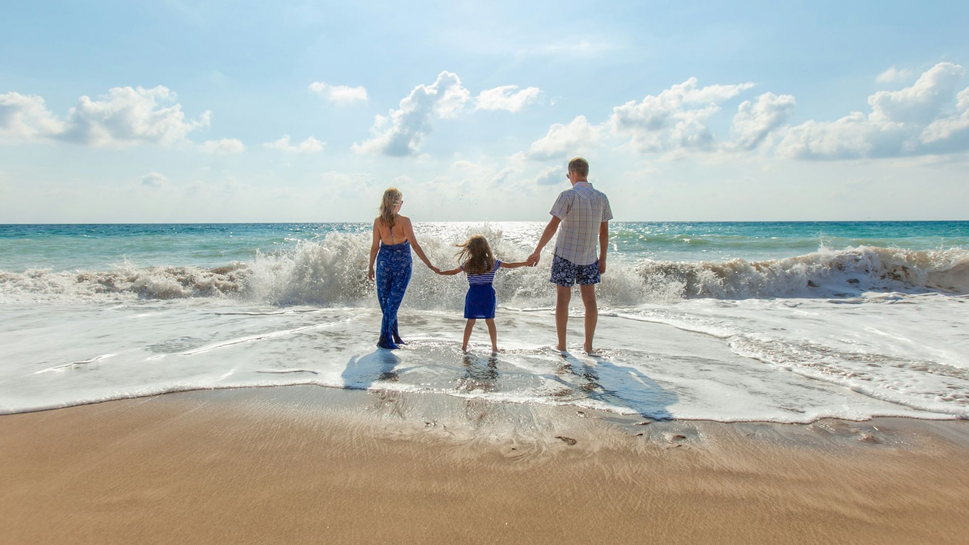 man, woman and child holding hands on seashore
