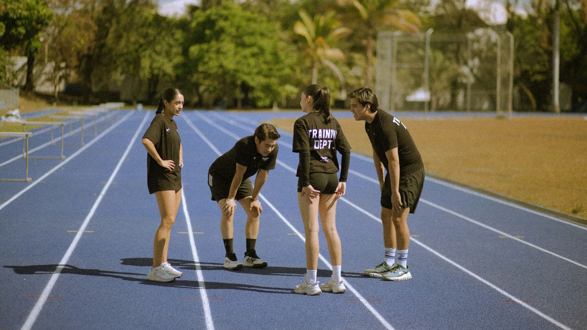 Four athletes in black on a blue running track