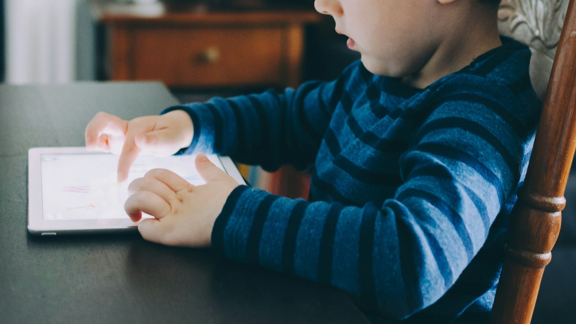 boy sitting on chair beside table using tablet computer