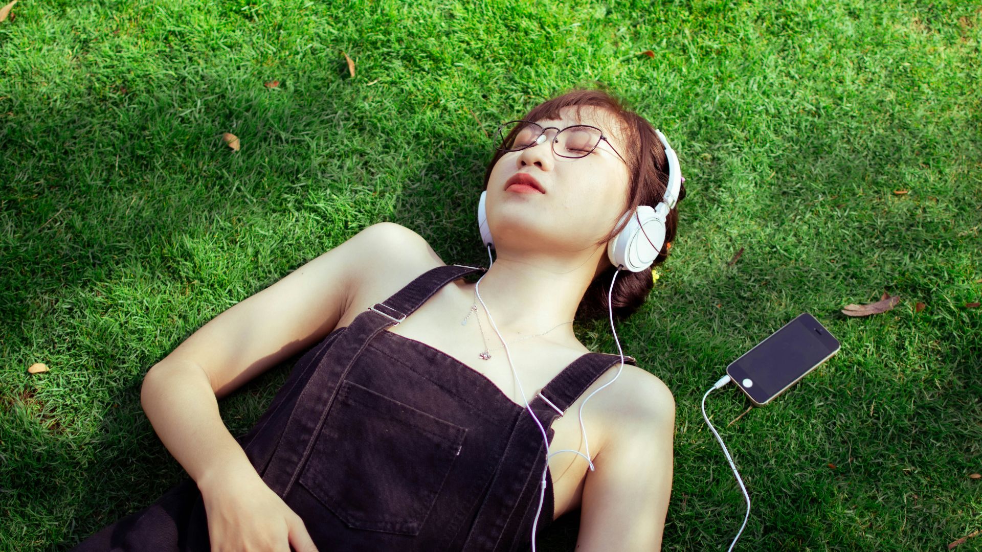 a woman laying on the grass listening to music