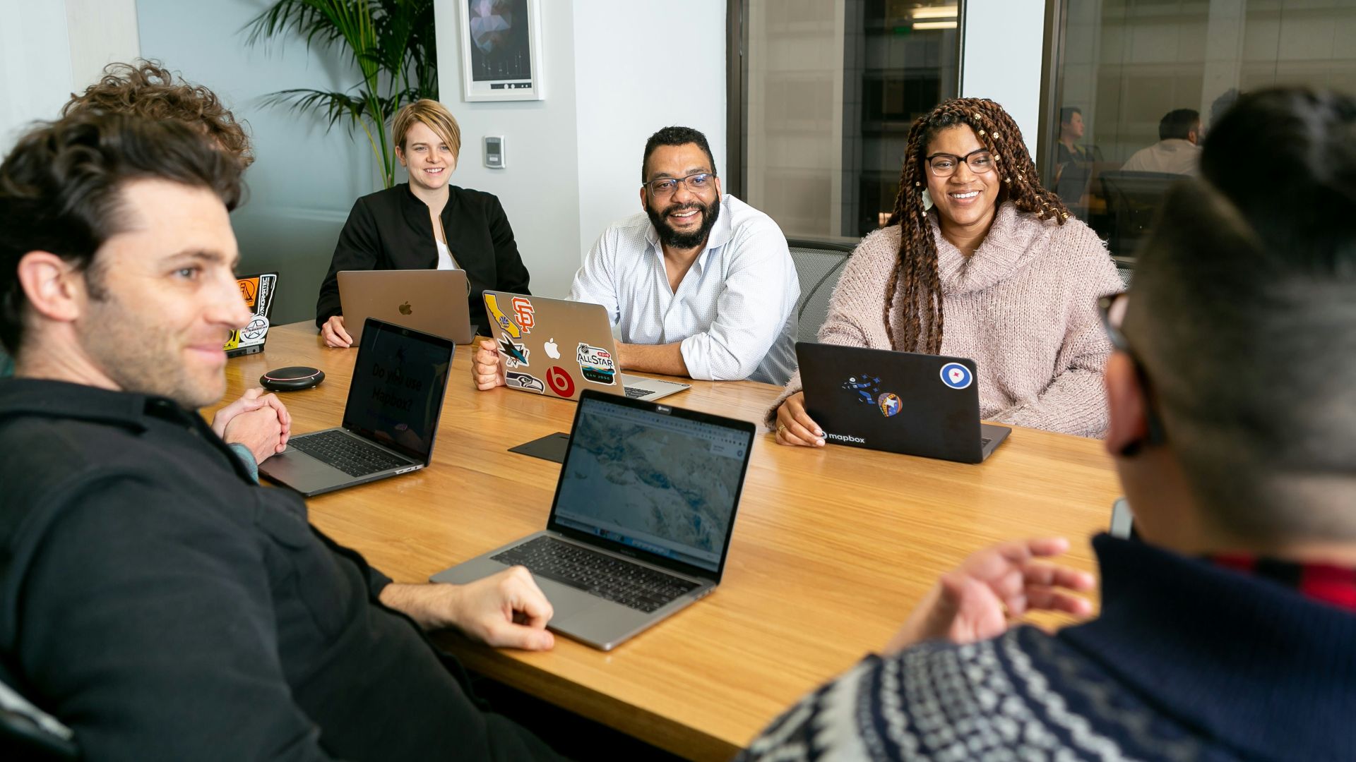 four people all on laptops, two men and two women, listen to person talking in a board meeting