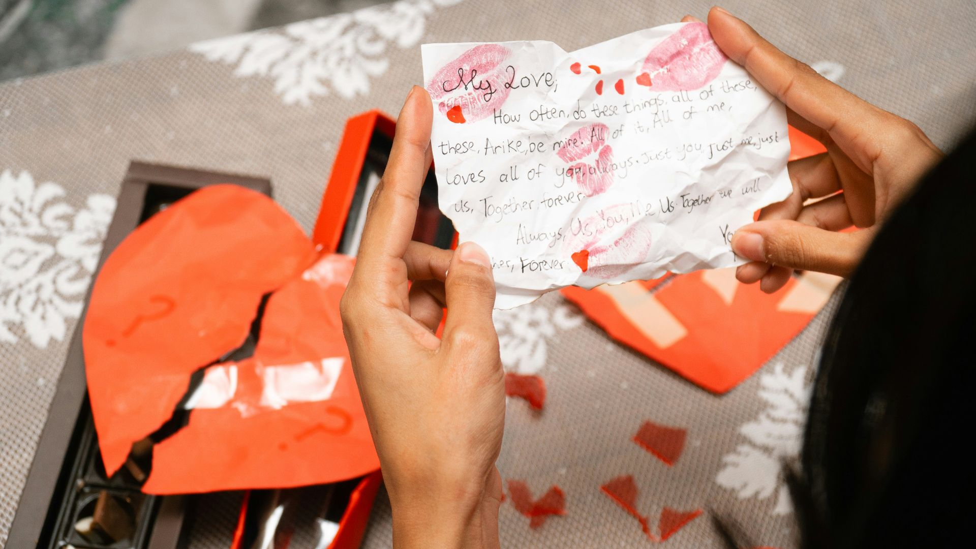 Hands holding a torn love letter near broken heart