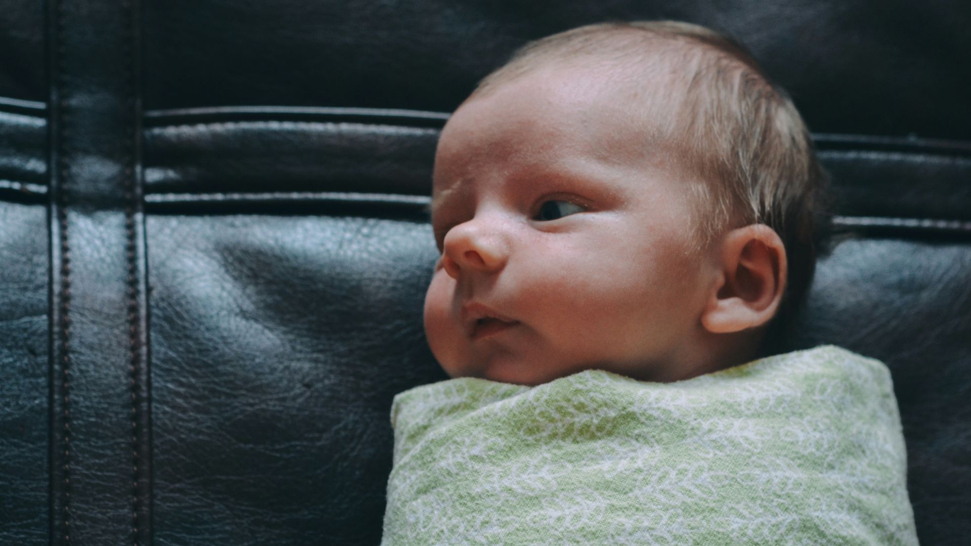 baby covered in green blanket on black leather surface
