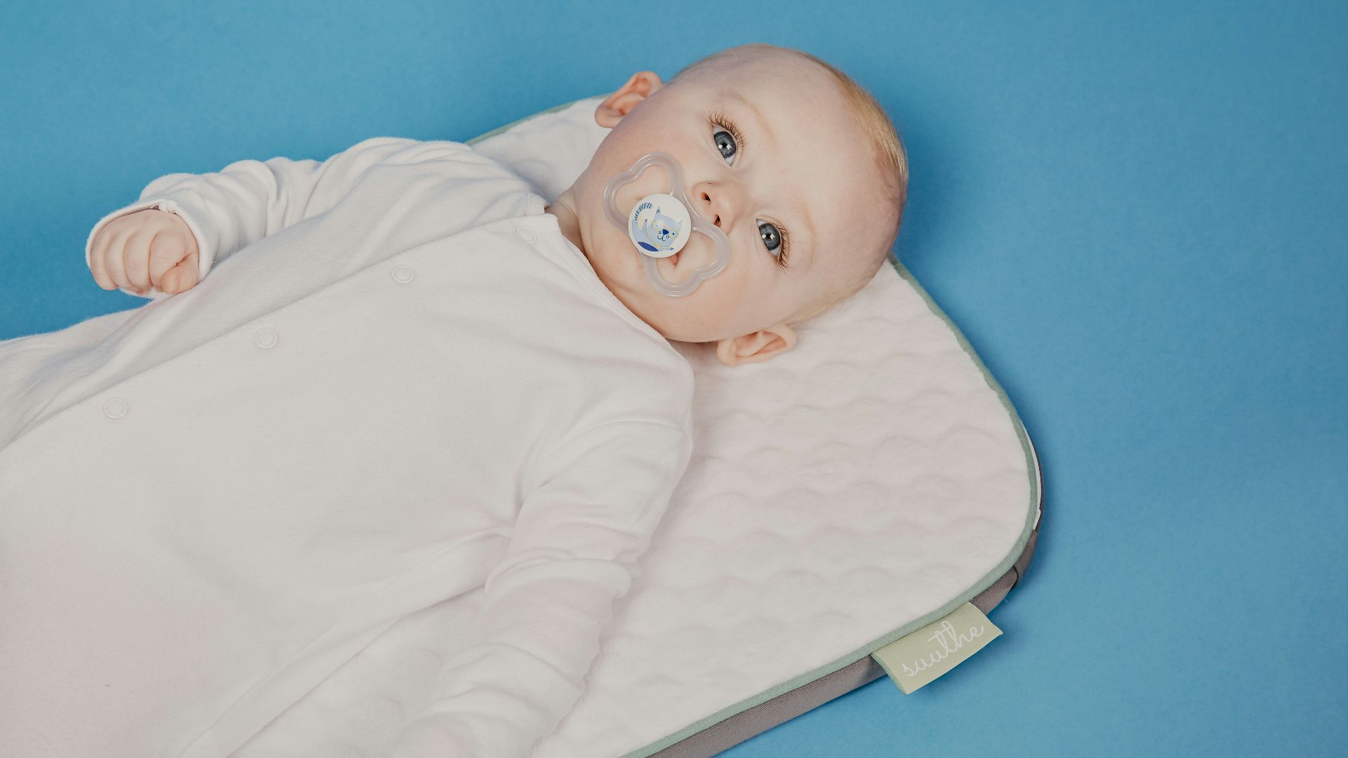baby in white onesie lying on bed