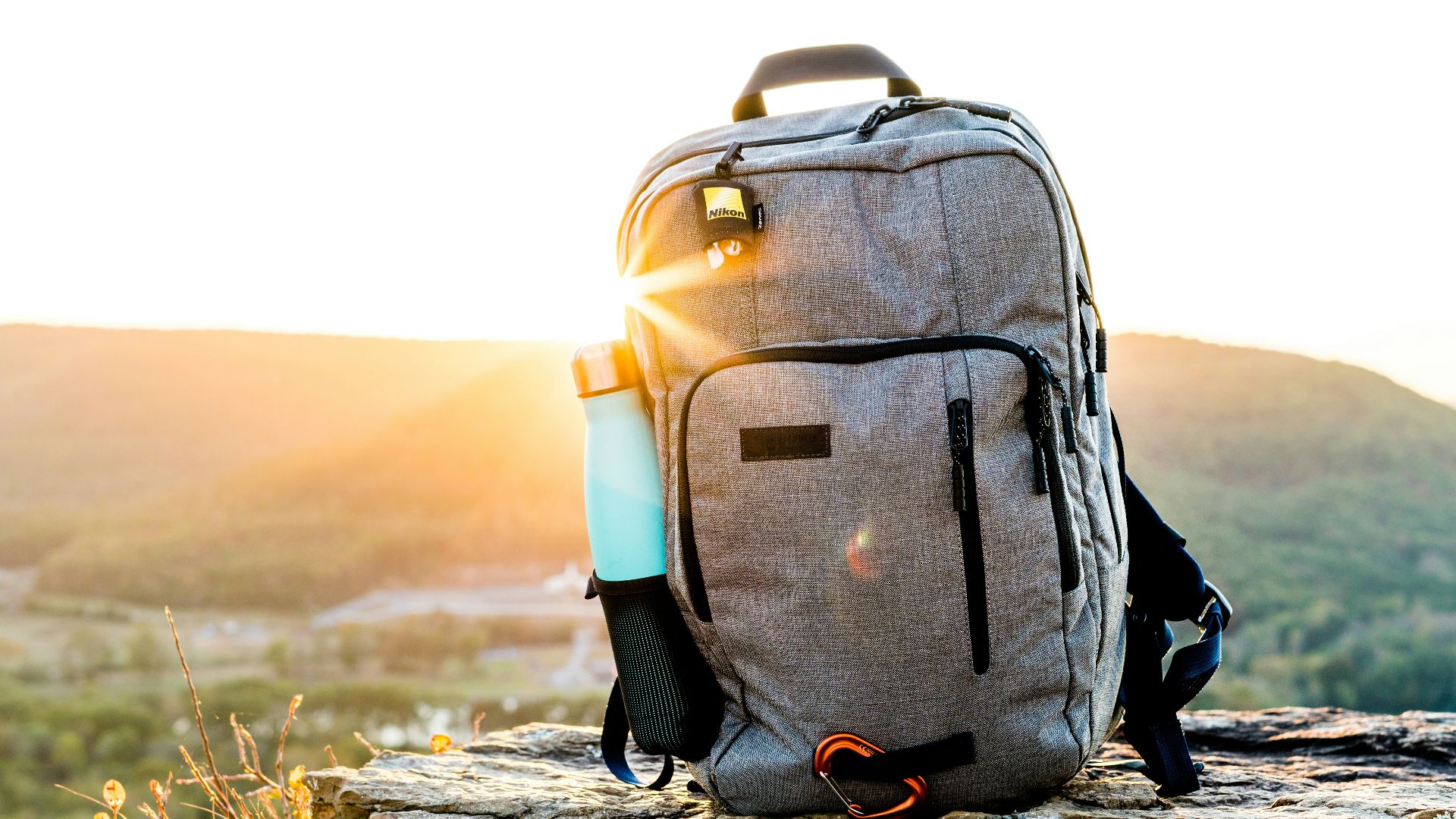grey and black hiking backpack and cyan tumbler on grey rock during sunset