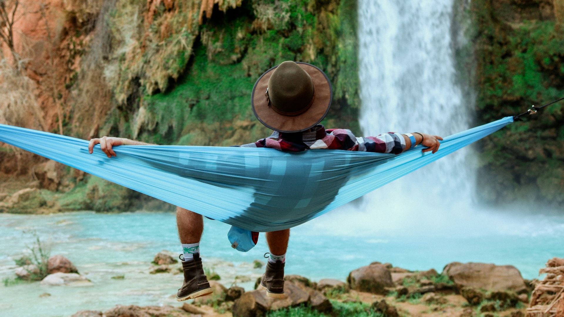 man lying on hammock near waterfalls