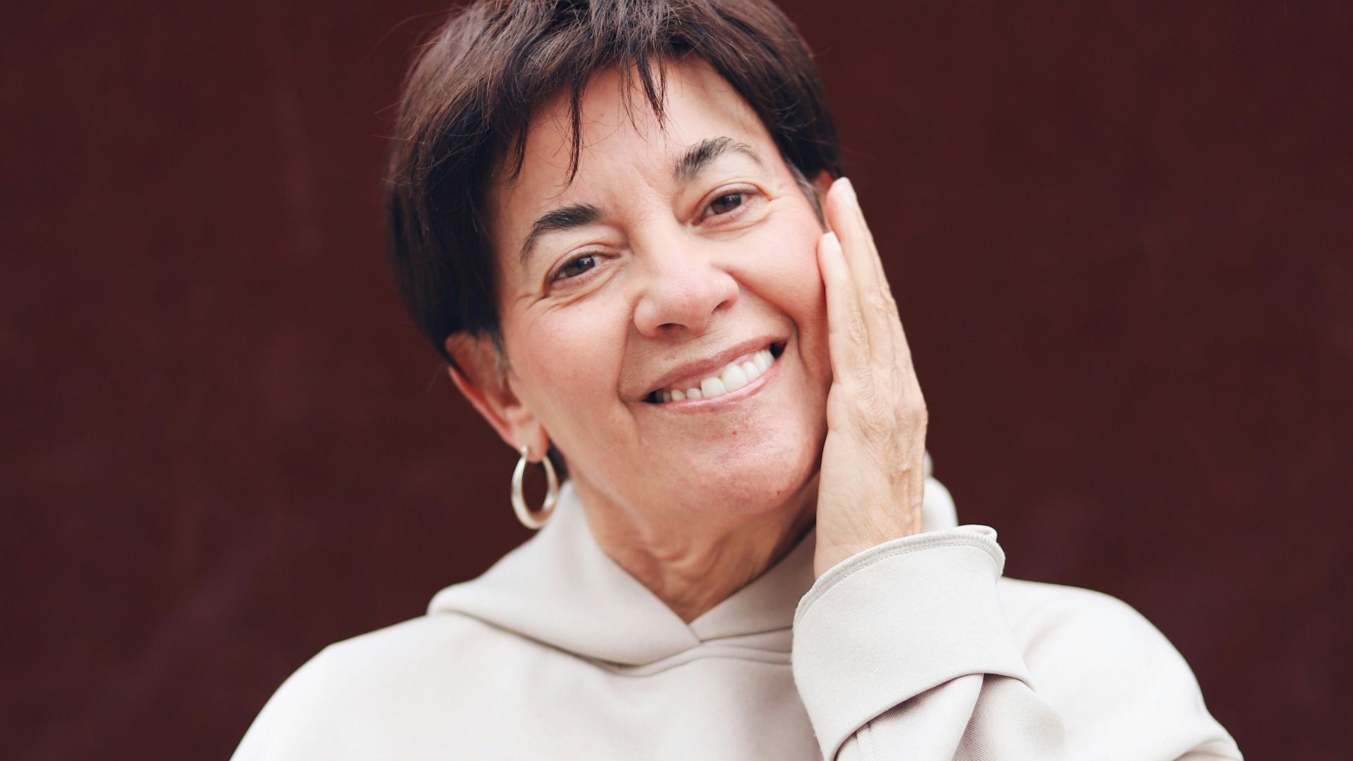 A woman in a white sweater is holding her hand up to her face