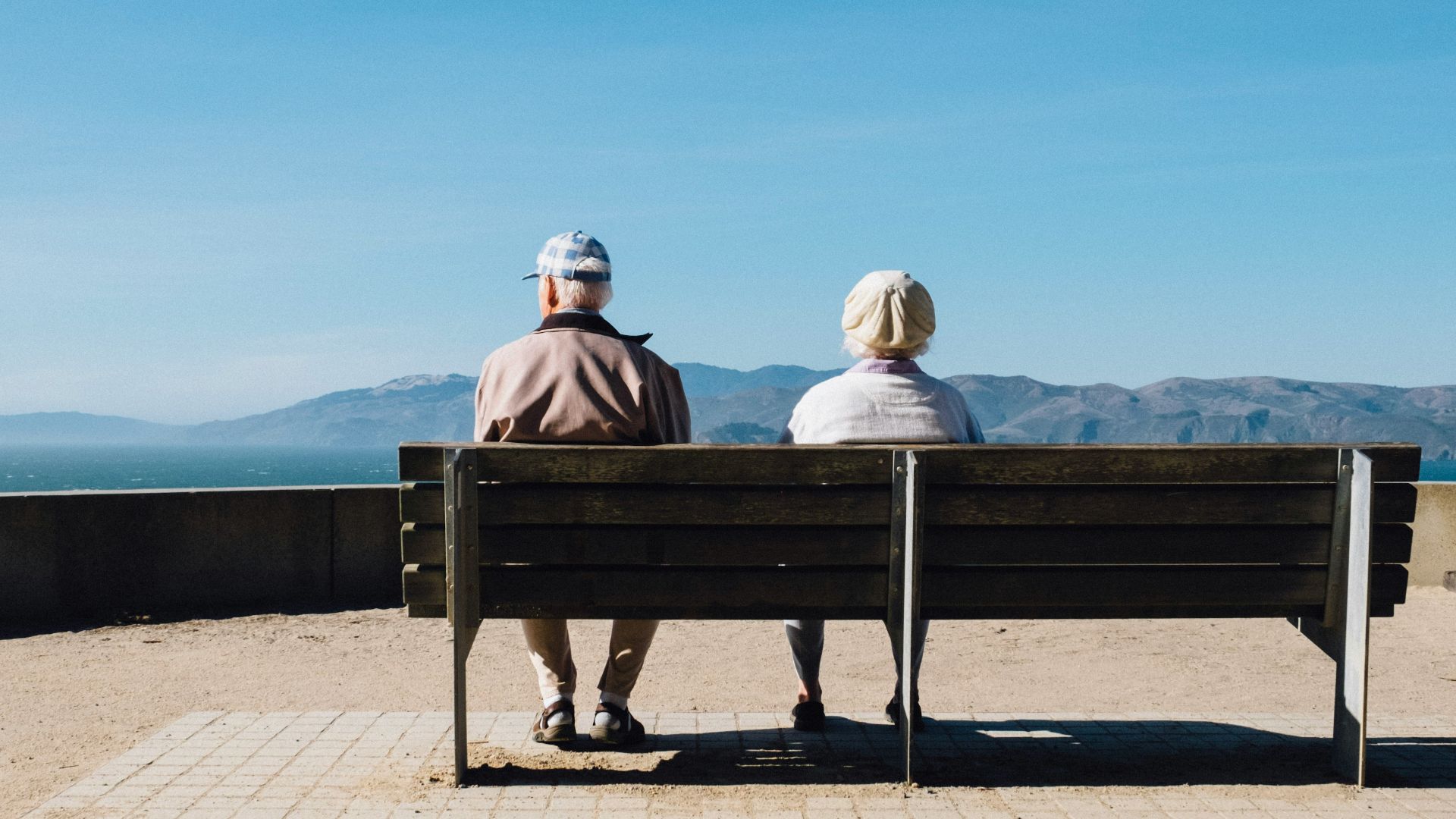 man and woman sitting on bench facing sea