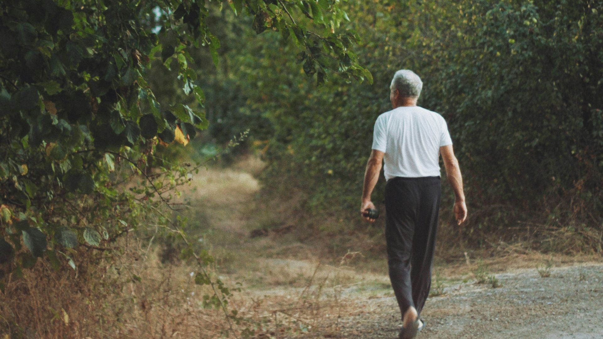 man in white shirt and black pants walking on dirt road