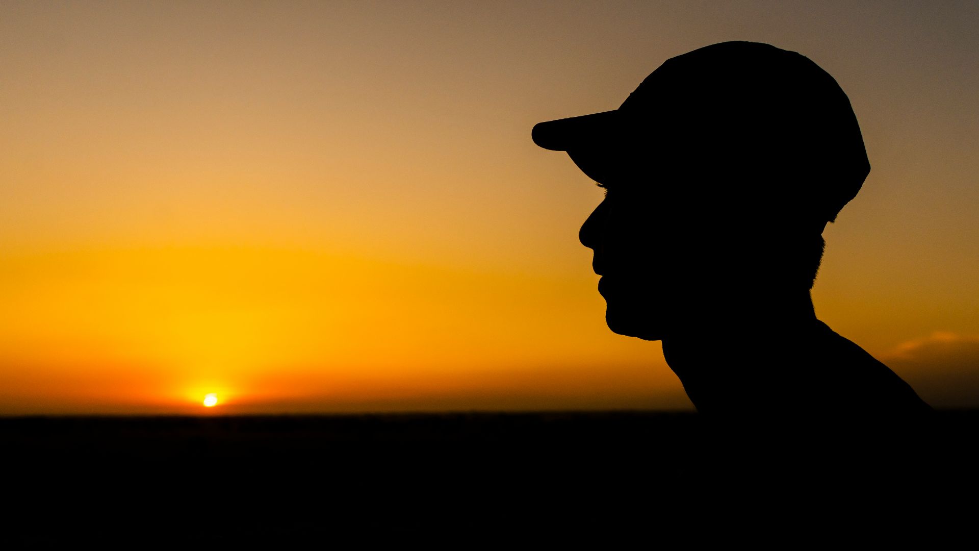a silhouette of a man wearing a hat at sunset
