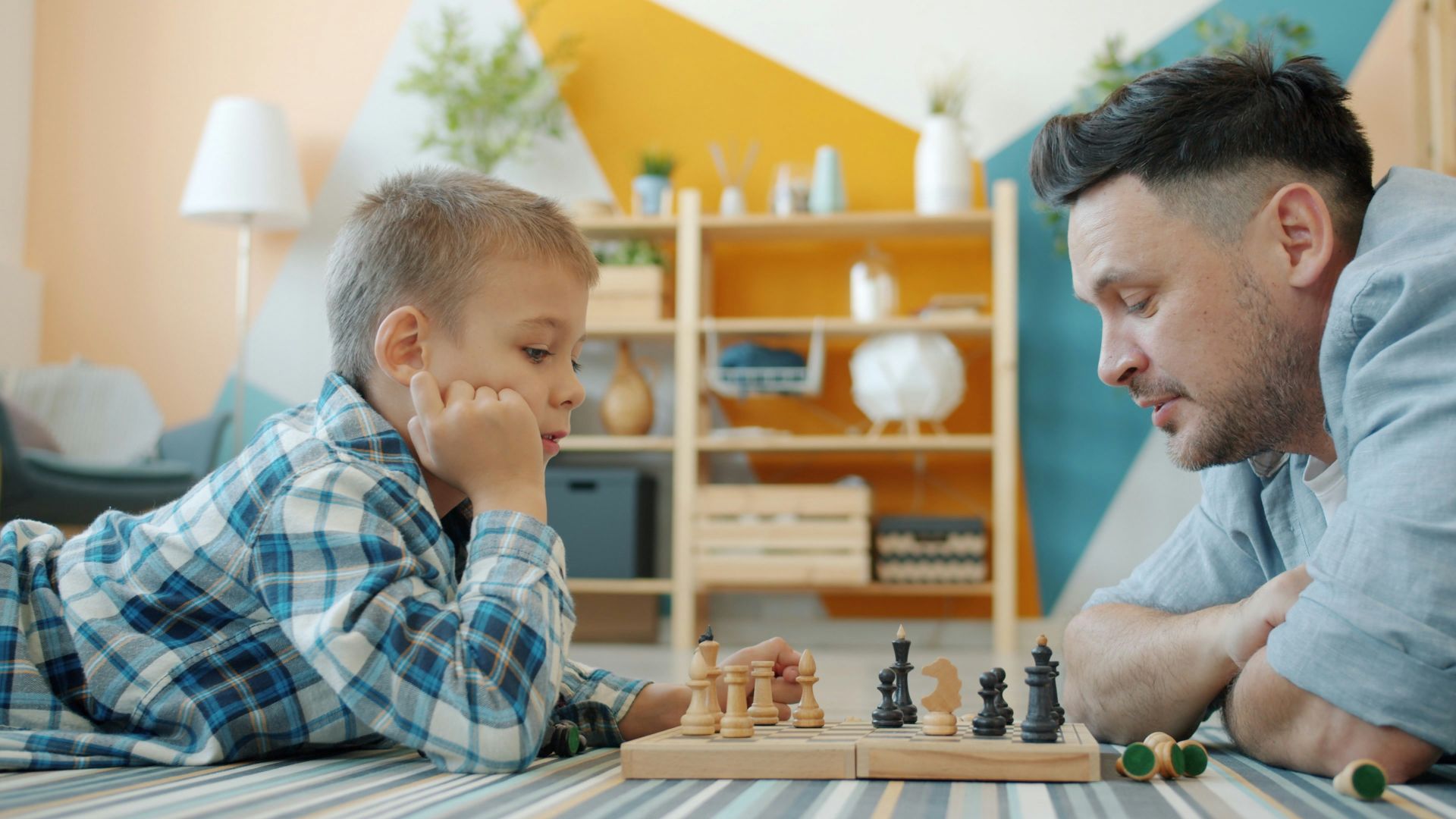 Father and son playing chess on the floor.