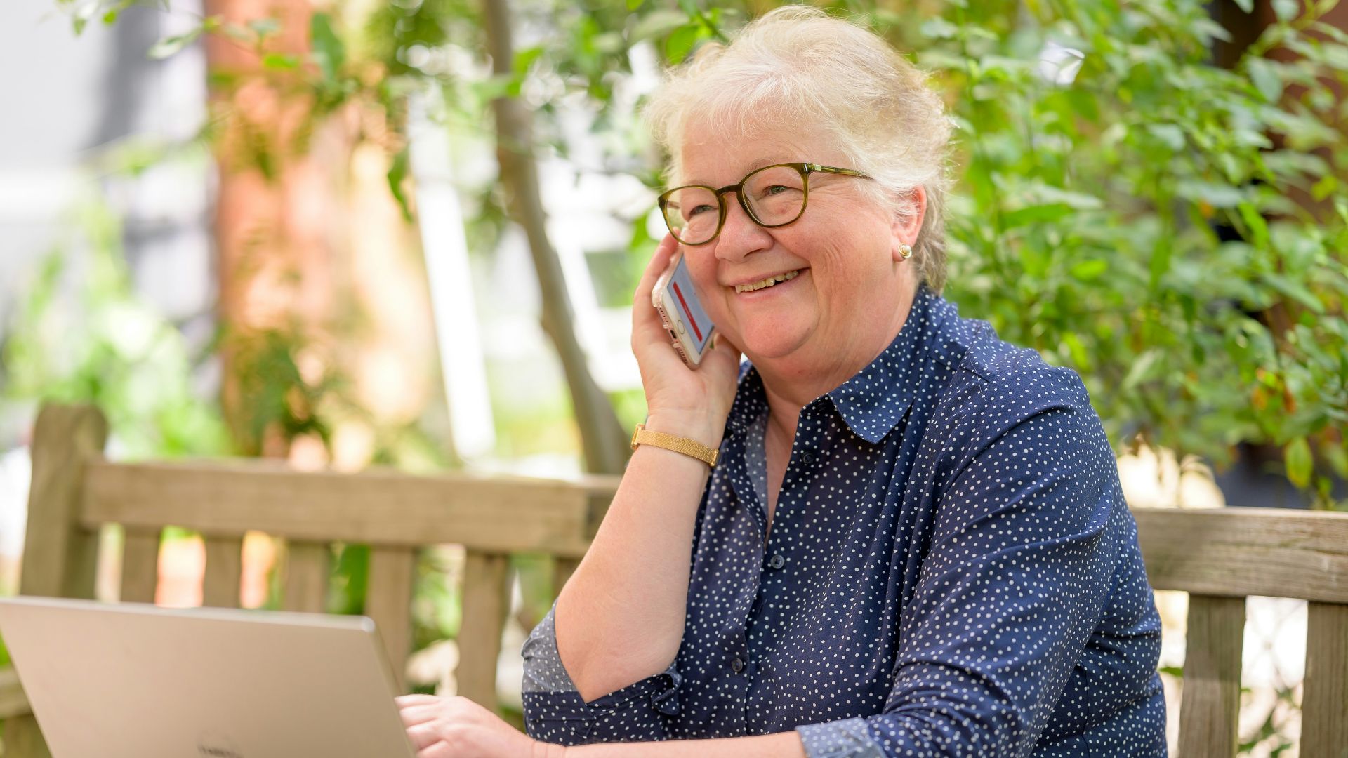 a woman on her phone while sitting at a table with a laptop