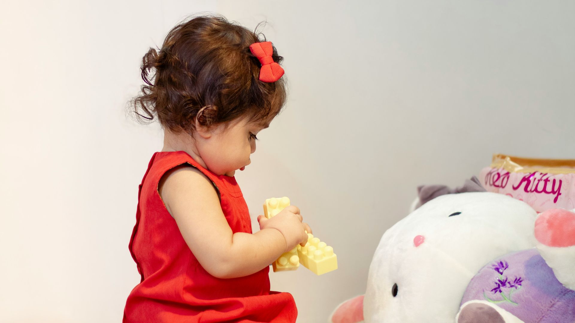 a little girl in a red dress playing with a stuffed animal