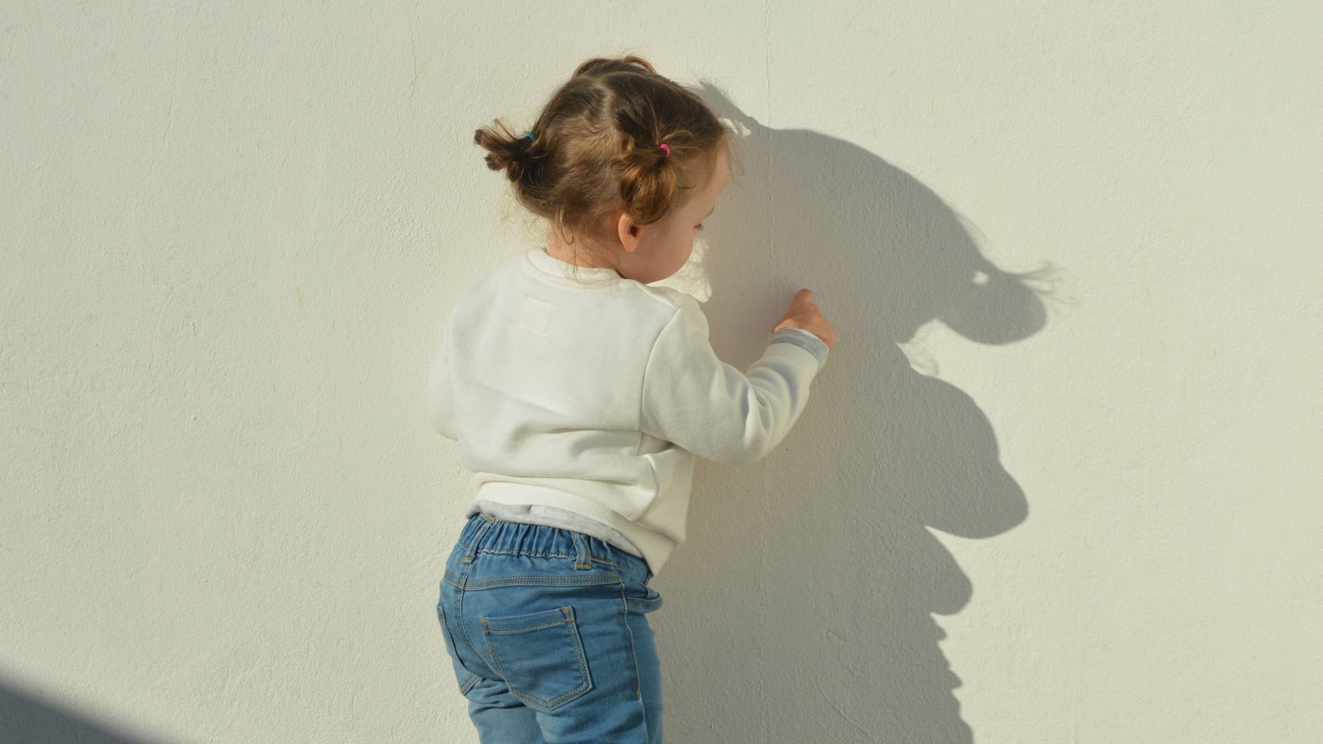 child touching white painted wall during daytime