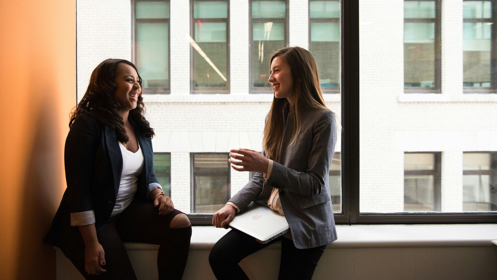 two woman sitting by the window laughing