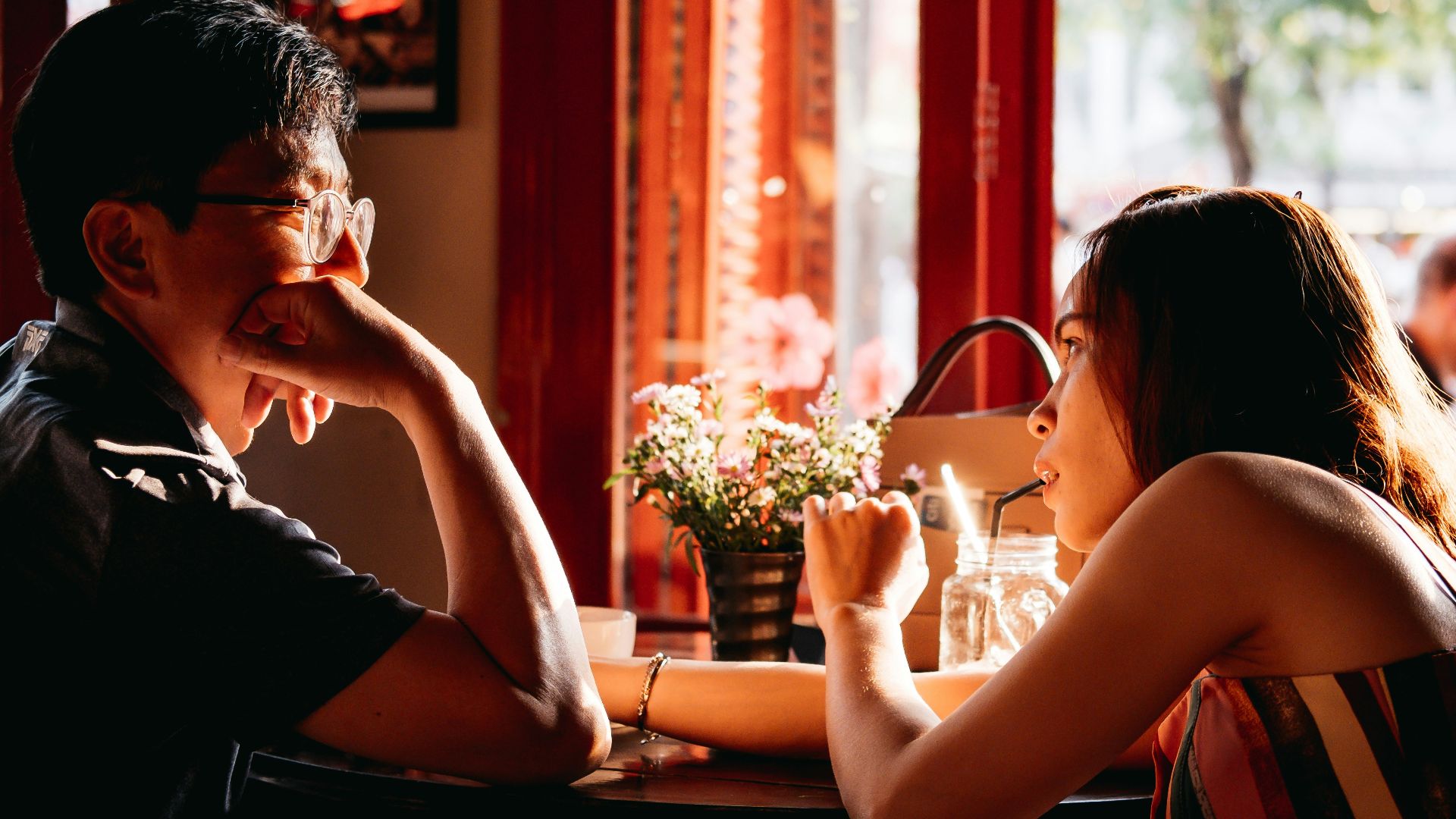 man wearing black collared top sitting on chair in front of table and woman wearing multicolored top