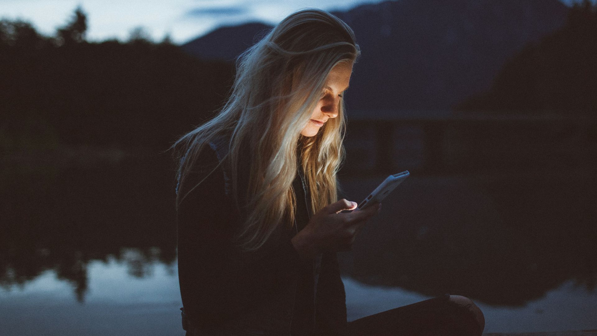woman looking at phone beside body of water