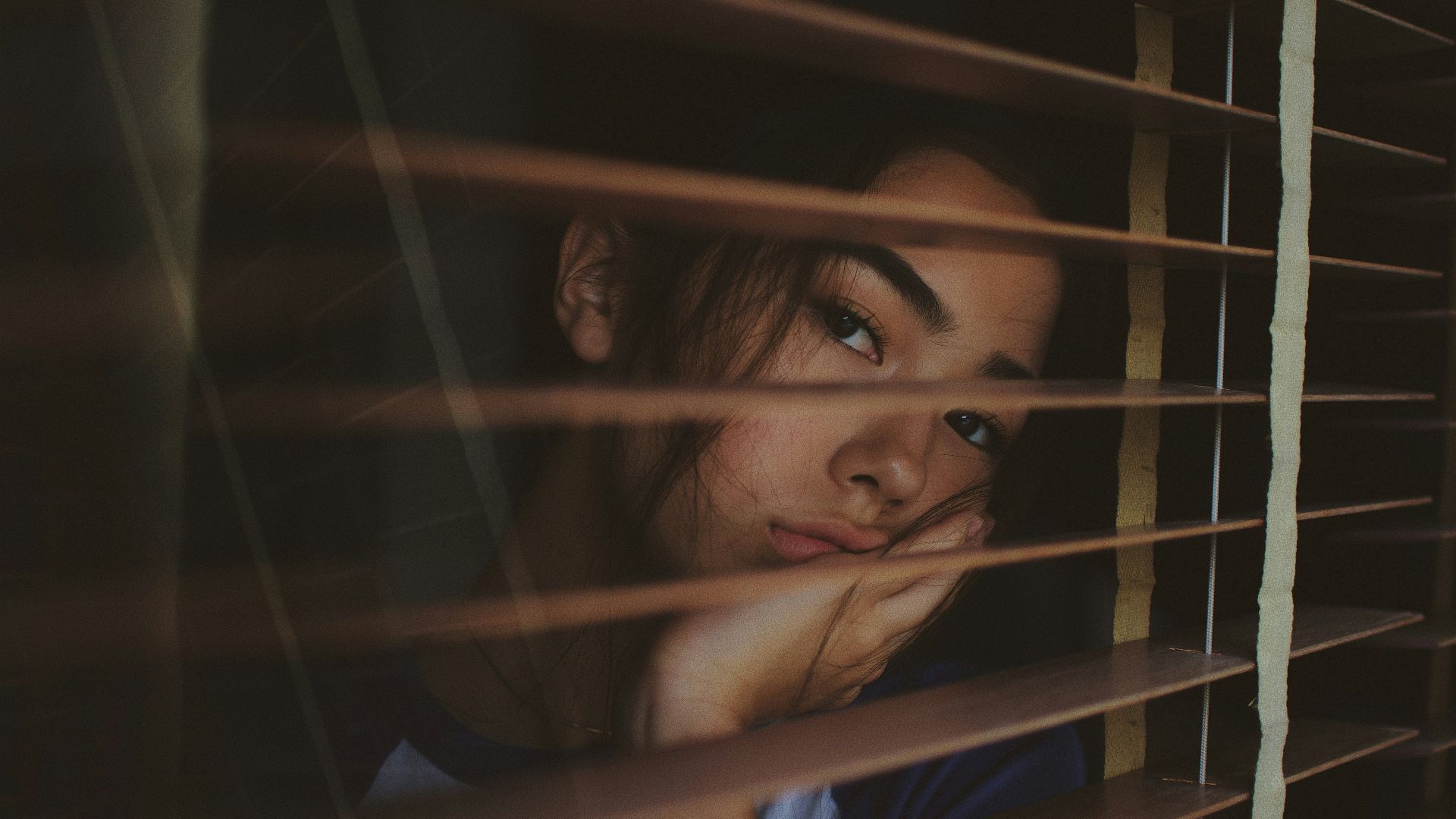 a woman looking out of a window with blinds