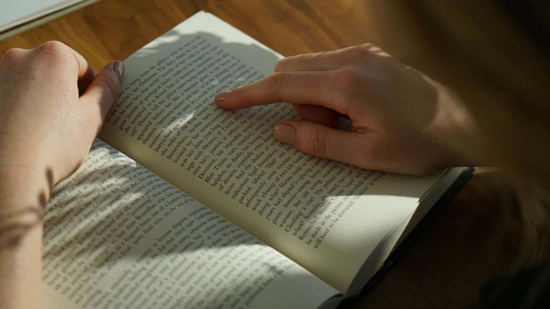 person reading book on brown wooden table taken at daytome