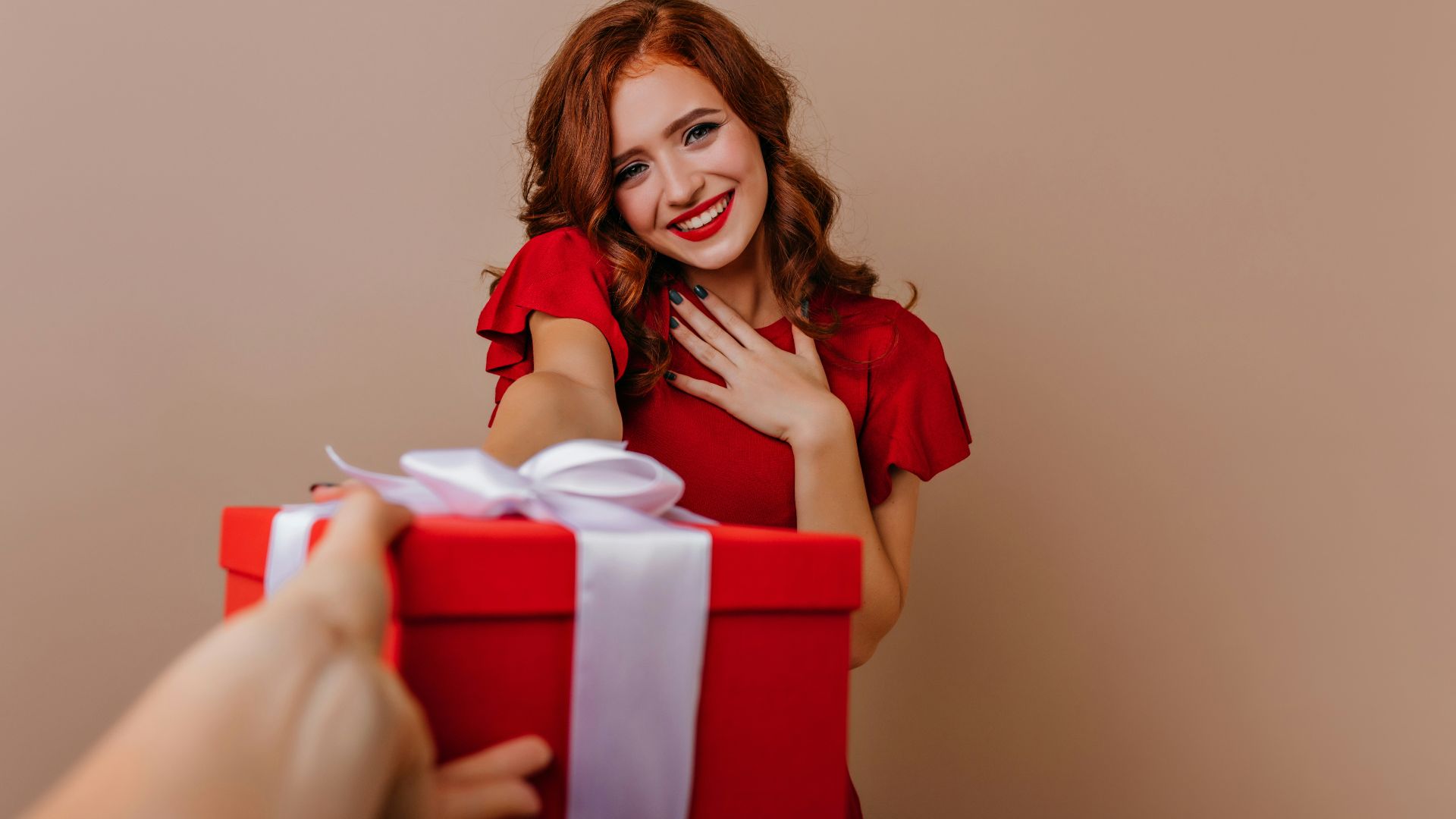 a woman holding a red gift box with a white ribbon