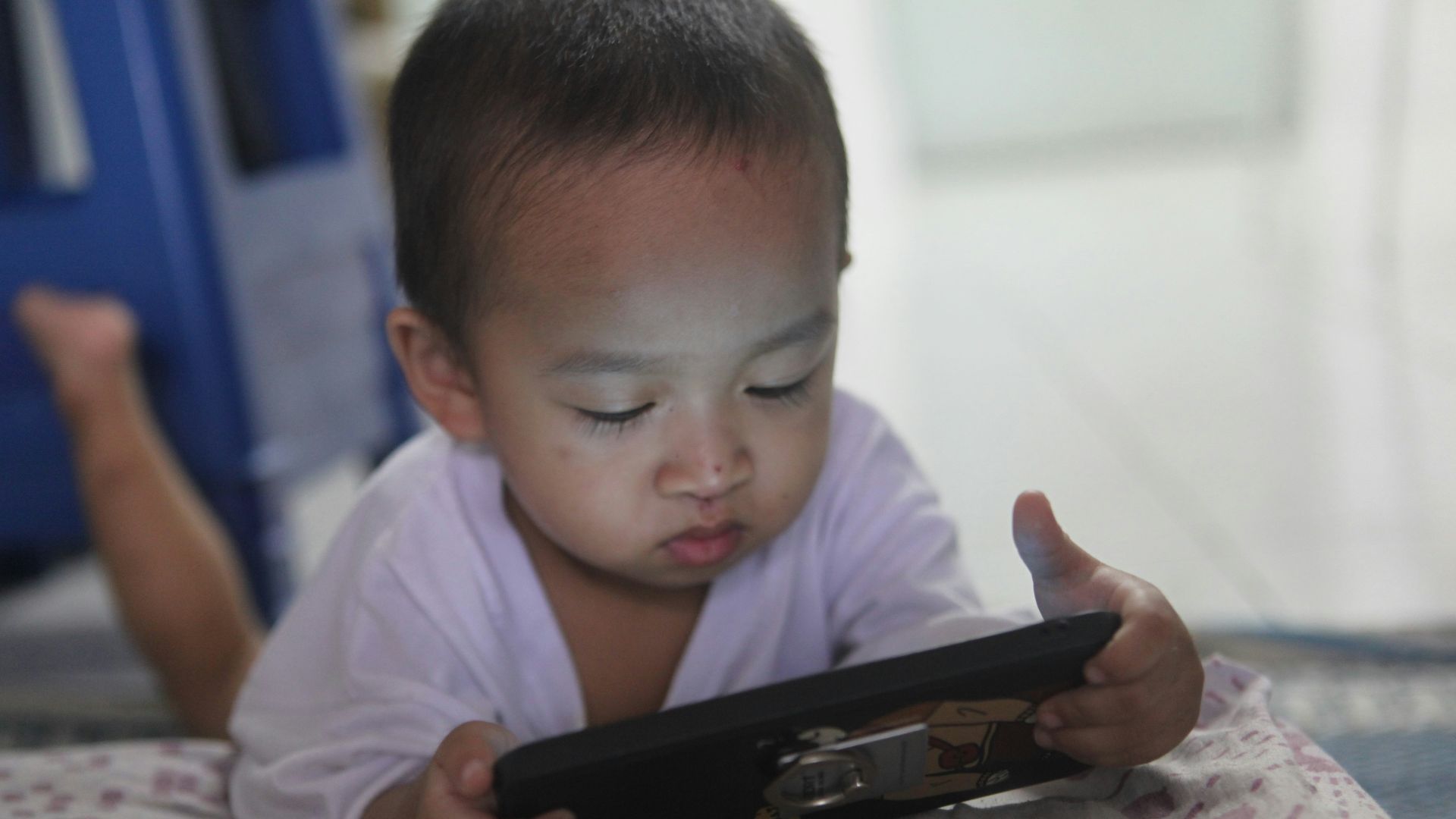 a small child laying on a bed playing with a tablet