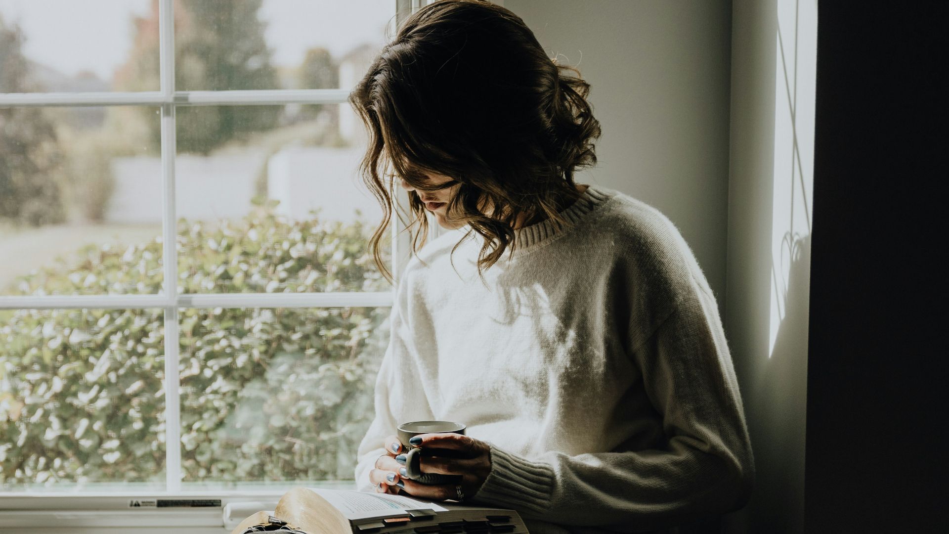 A woman sitting on a window sill reading a book