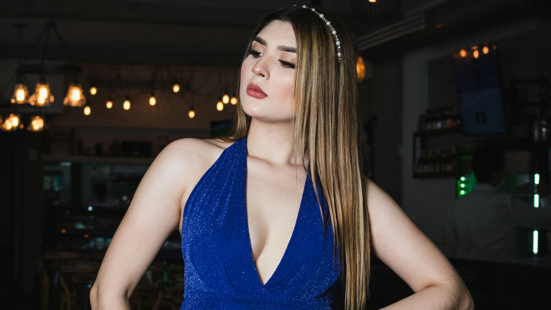 Woman in a sparkling blue halter dress poses indoors.