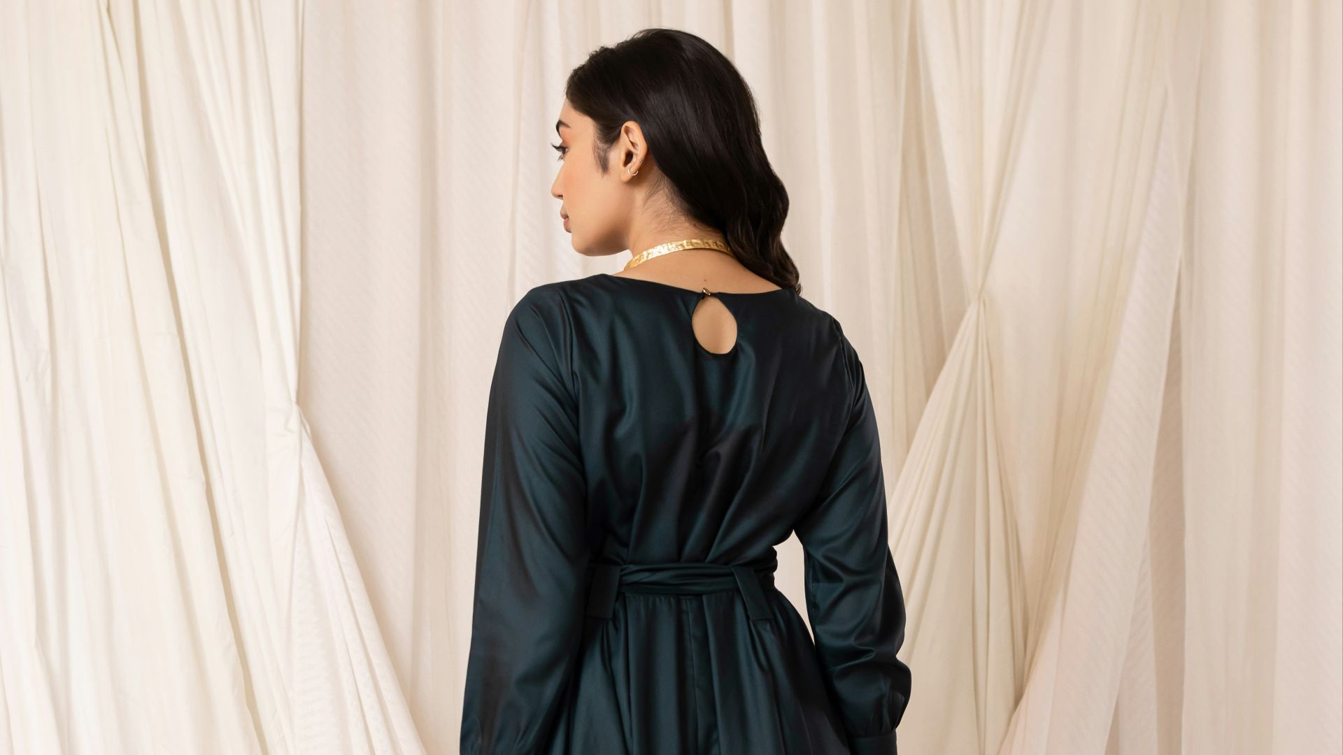 Woman in dark green dress with belt and keyhole back.