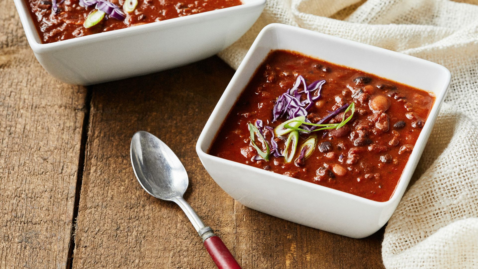 two bowls of chili and a spoon on a wooden table