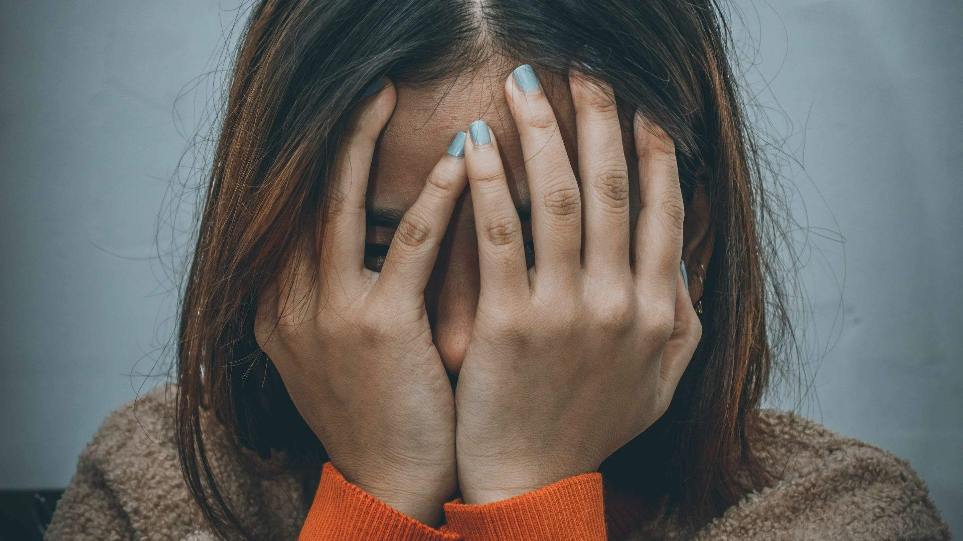 woman in brown sweater covering her face with her hand