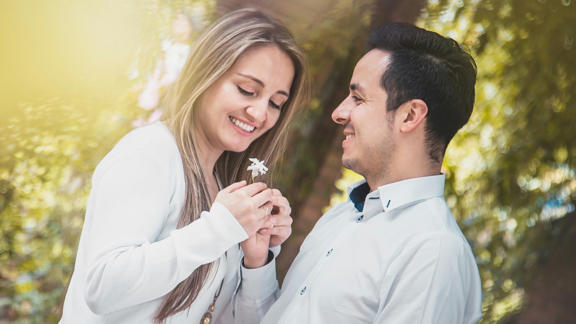 man giving white flower to woman surrounded by green trees