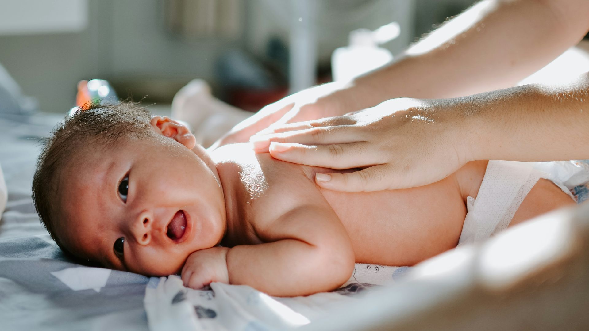 baby laying on bed while woman massaging his back