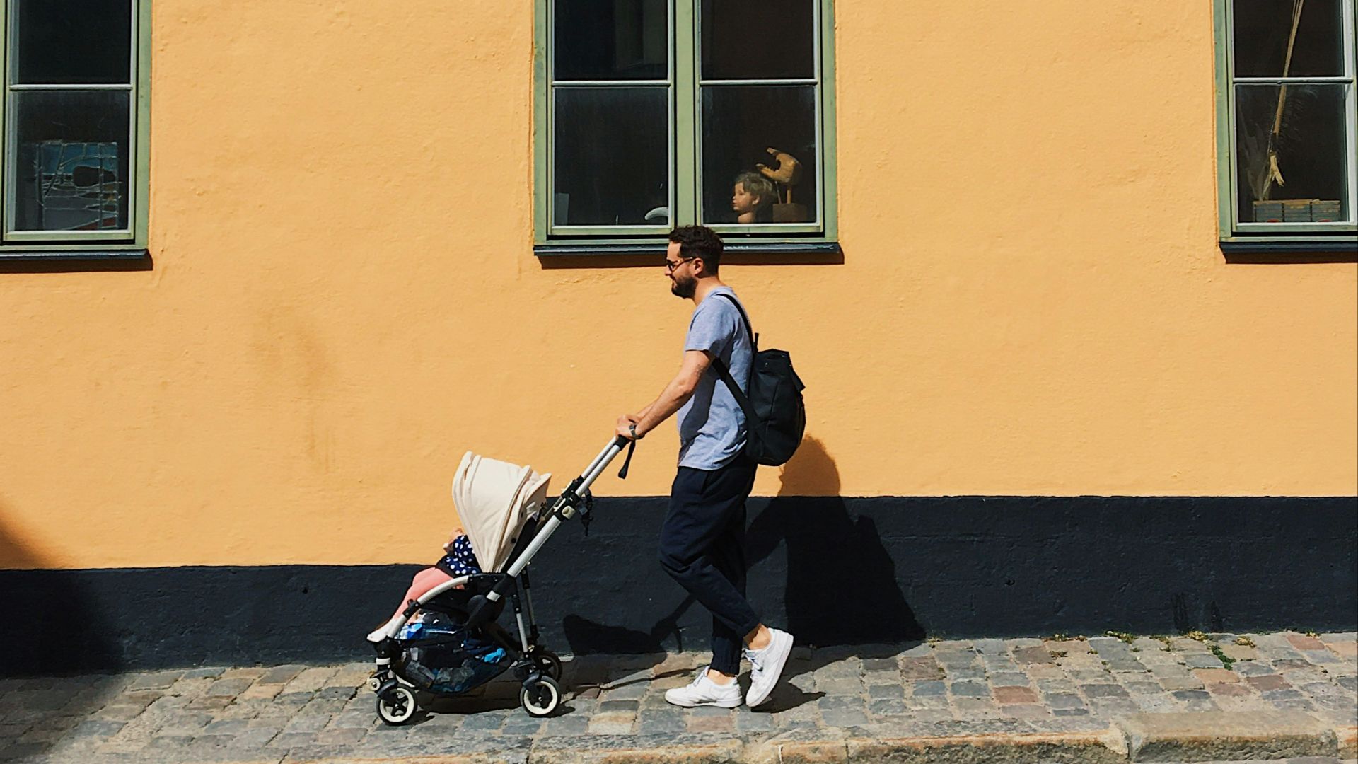 man in black suit sitting on black bench beside yellow concrete building during daytime