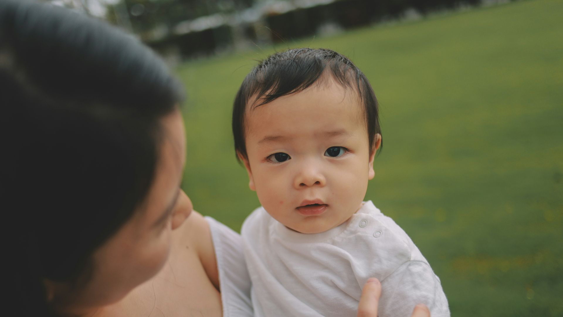A mother holds her baby in a park.