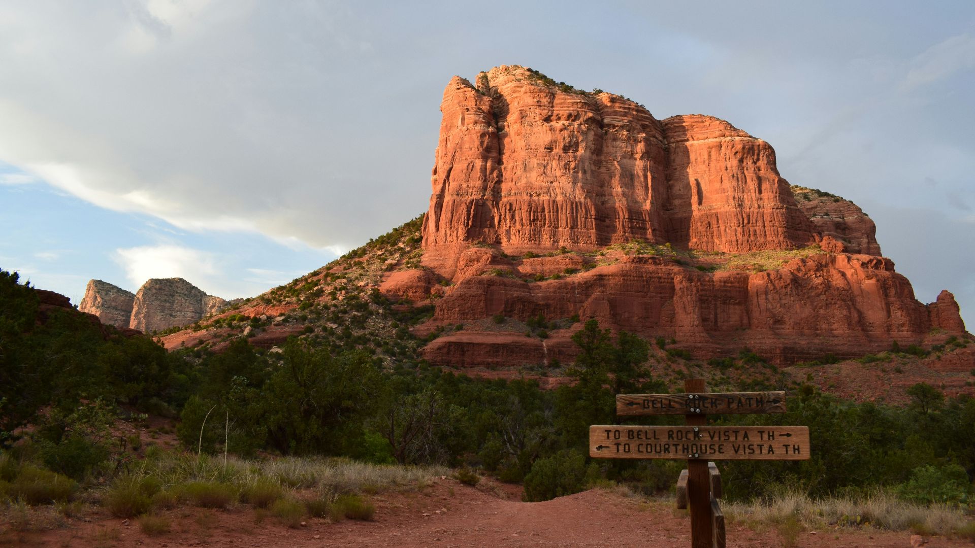 a sign in front of a rock formation with Bell Rock in the background