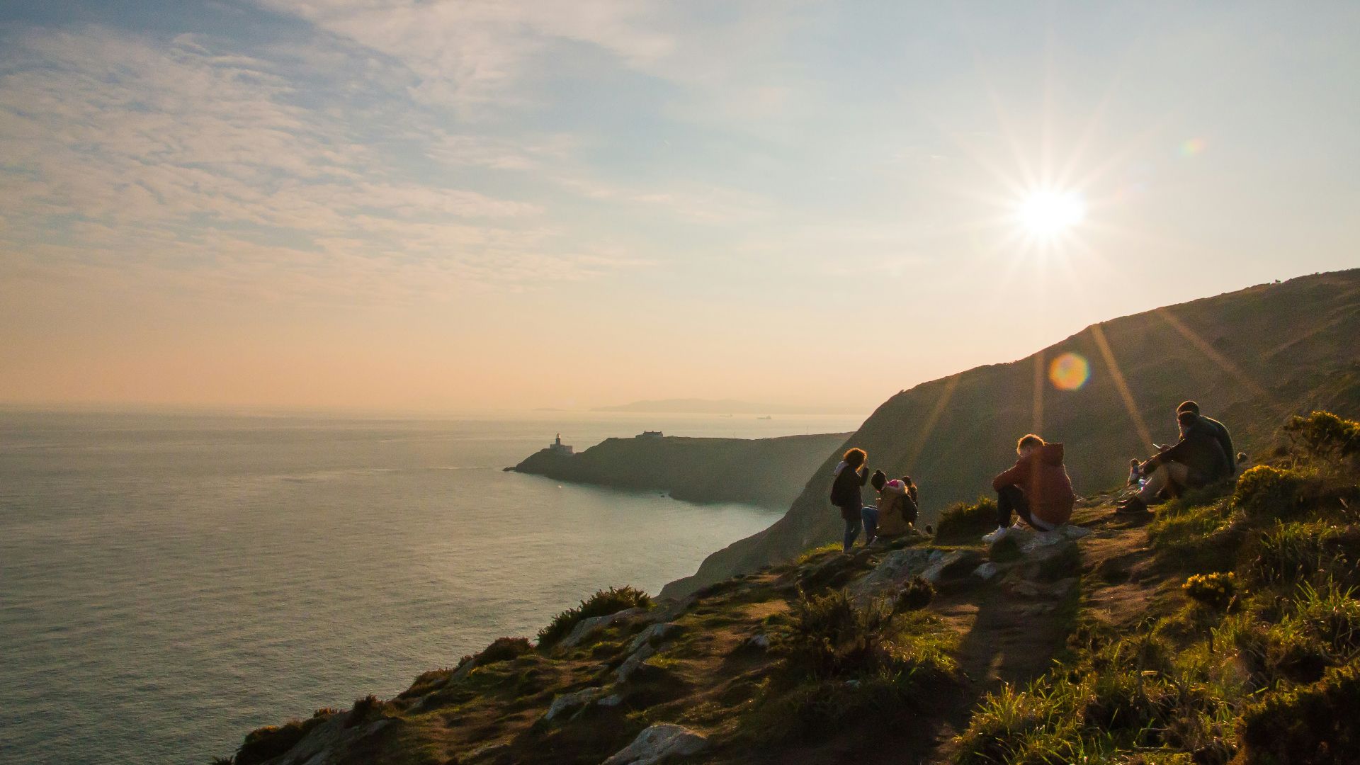 group of people sitting on grass field in front of body of water