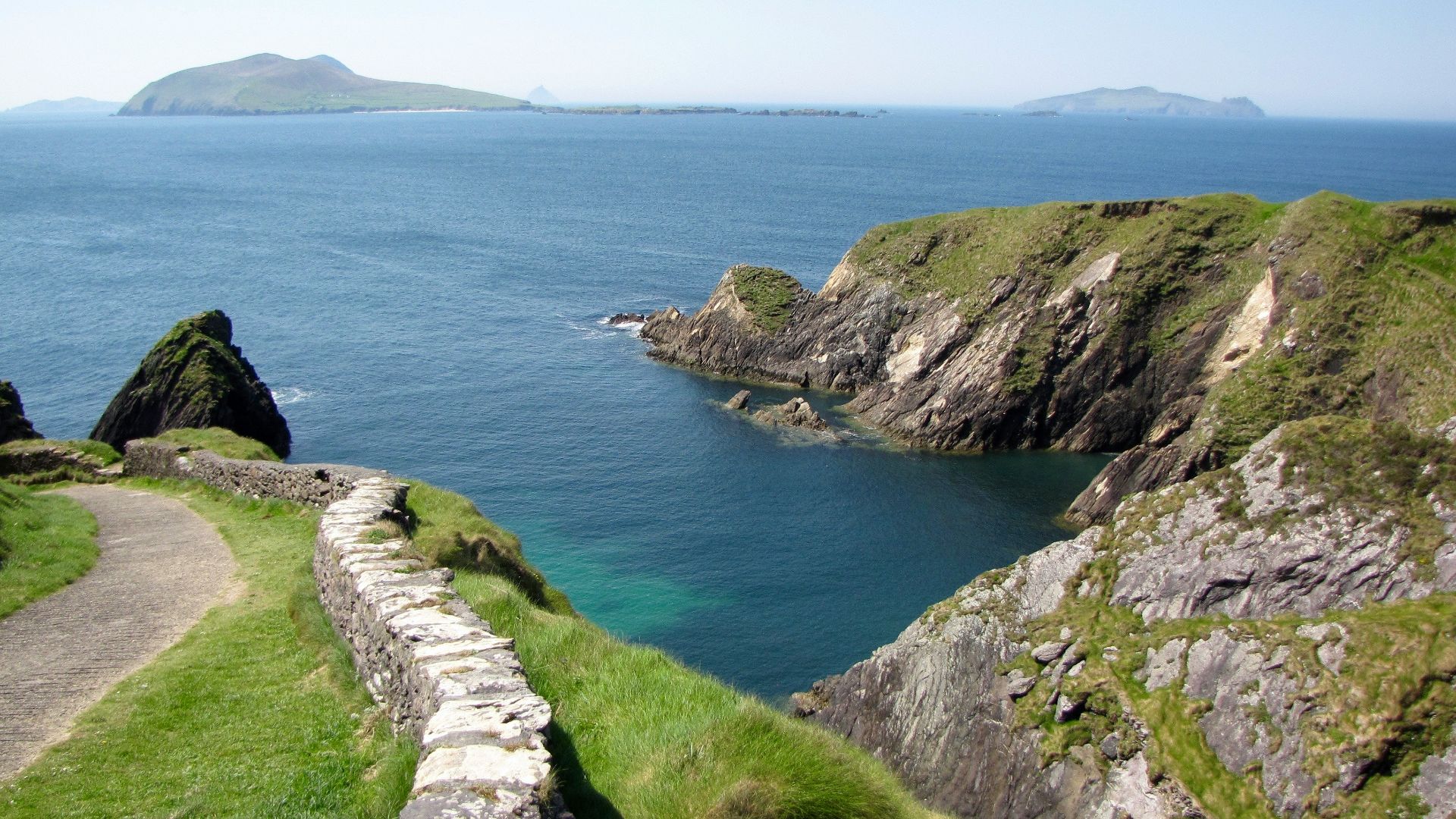 Coastal cliff path overlooking a calm blue bay.
