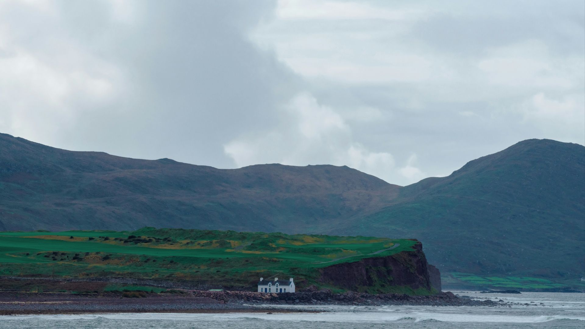 a house on the shore of a body of water with mountains in the background