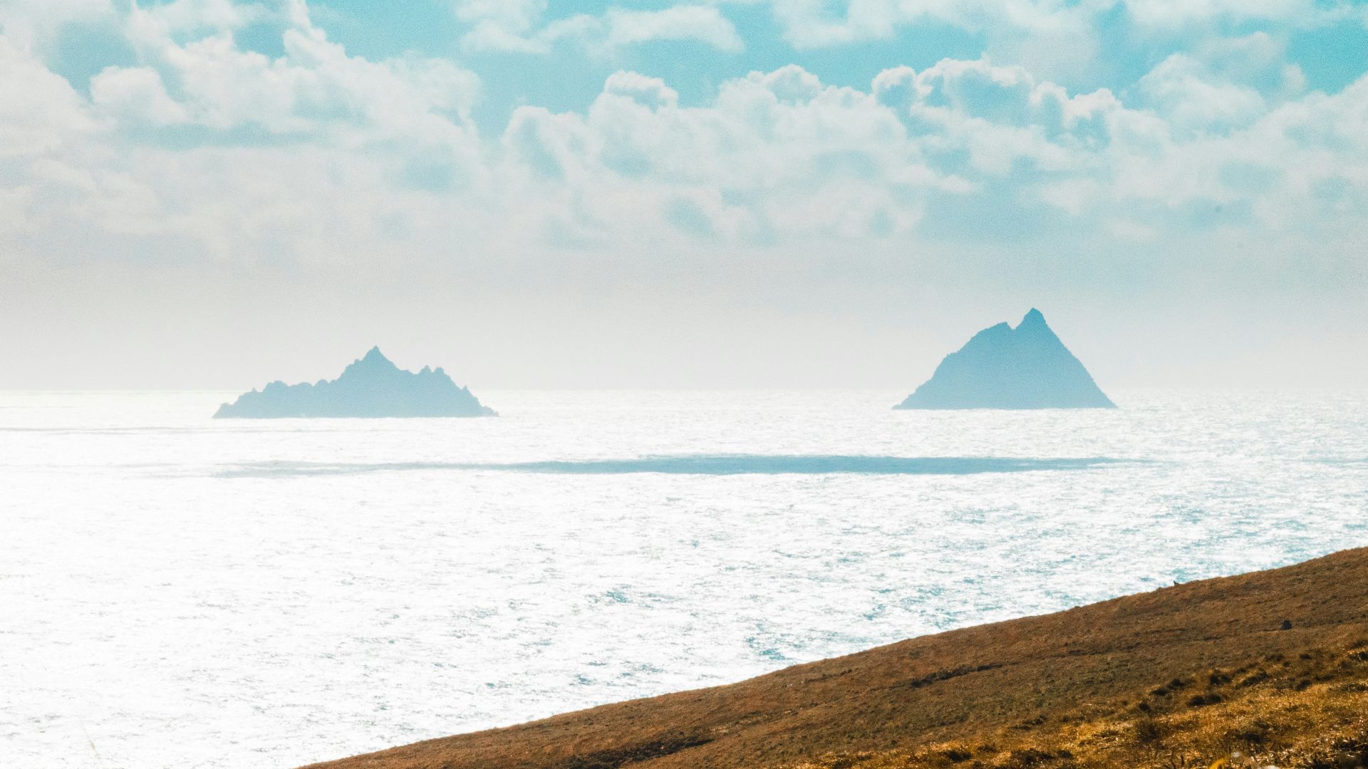 brown mountain near body of water under white clouds and blue sky during daytime