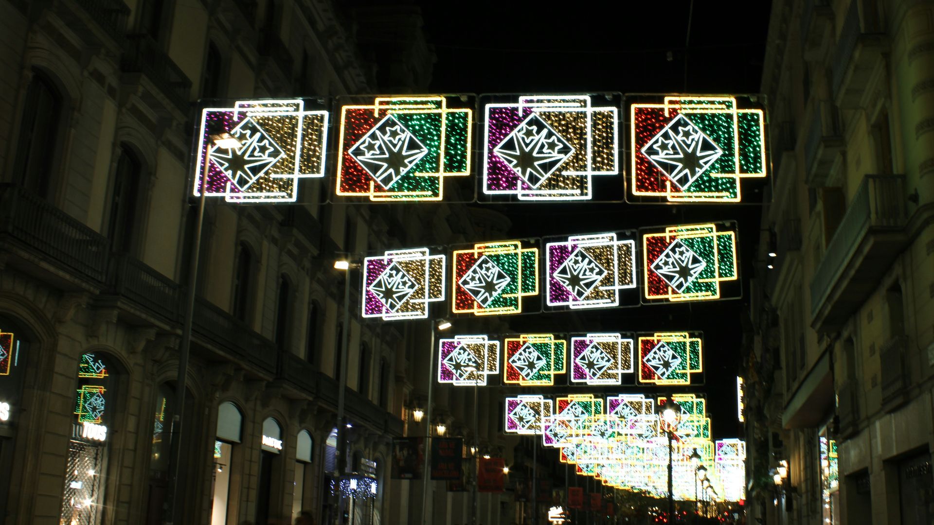 A group of people walking down a street next to tall buildings