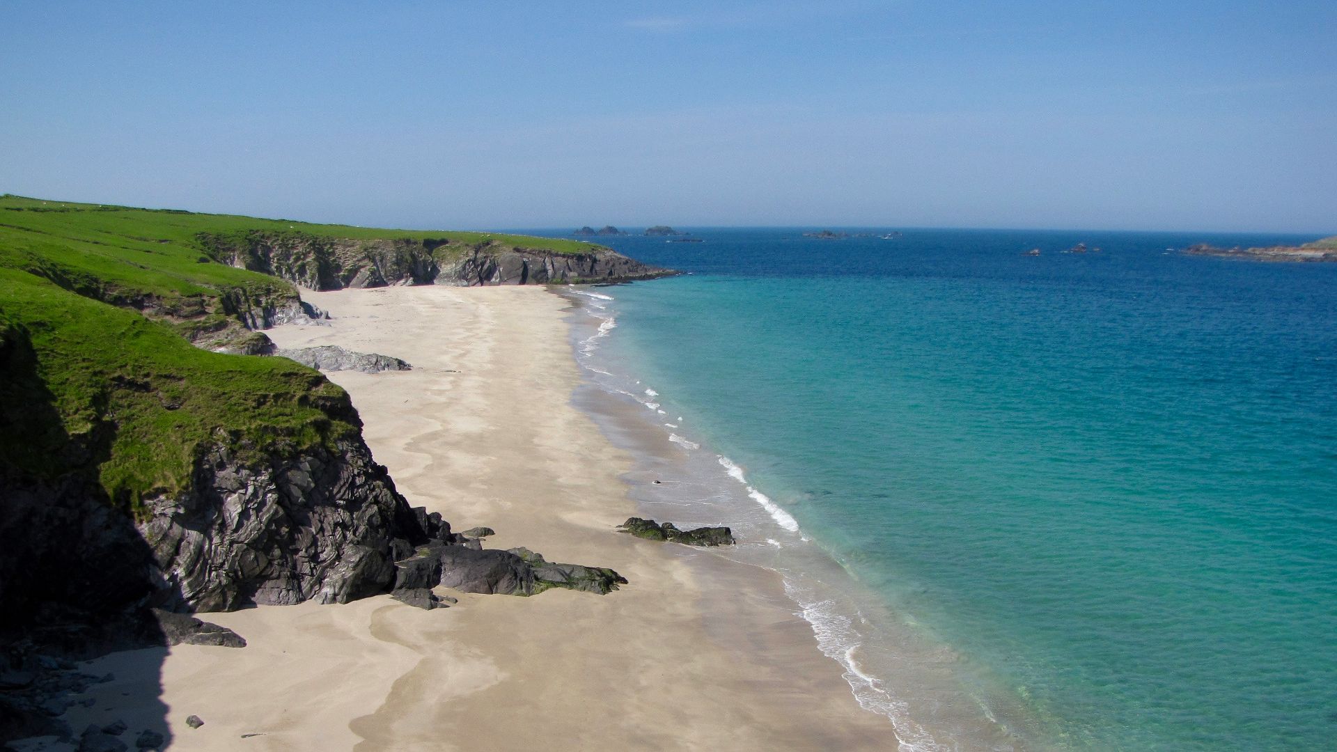 Sandy beach with turquoise water and green cliffs.