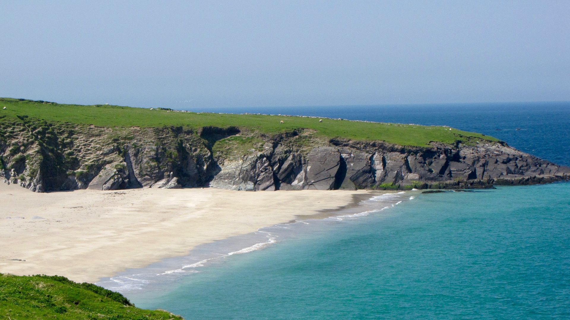 Sandy beach with cliffs and turquoise ocean water.