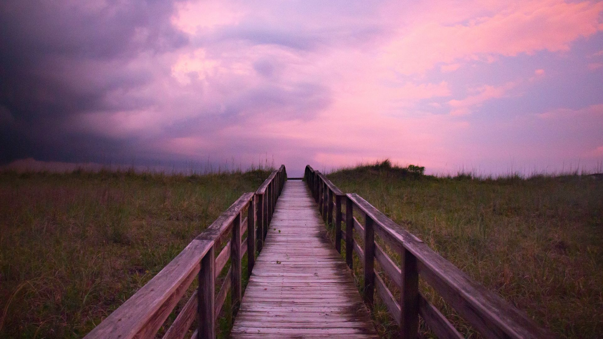 brown wooden bridge over green grass field under white clouds