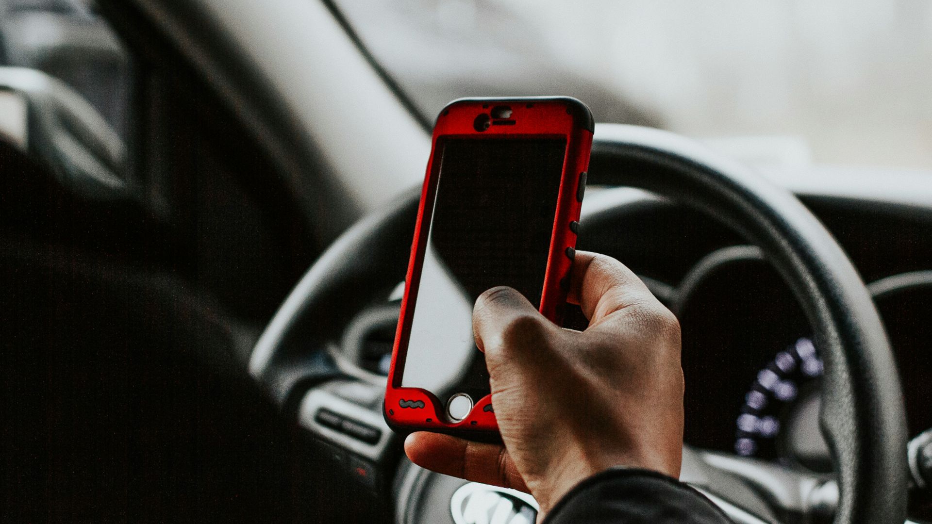 person holding red smartphone sitting in front of vehicle steering wheel