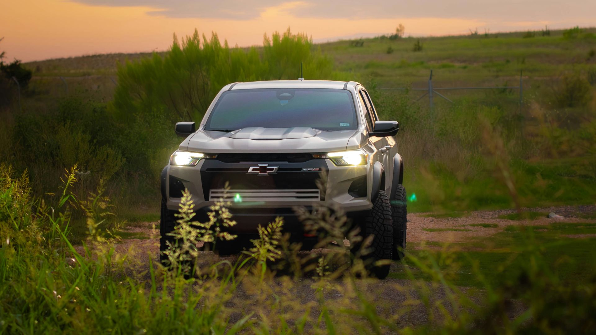 A silver truck driving down a dirt road