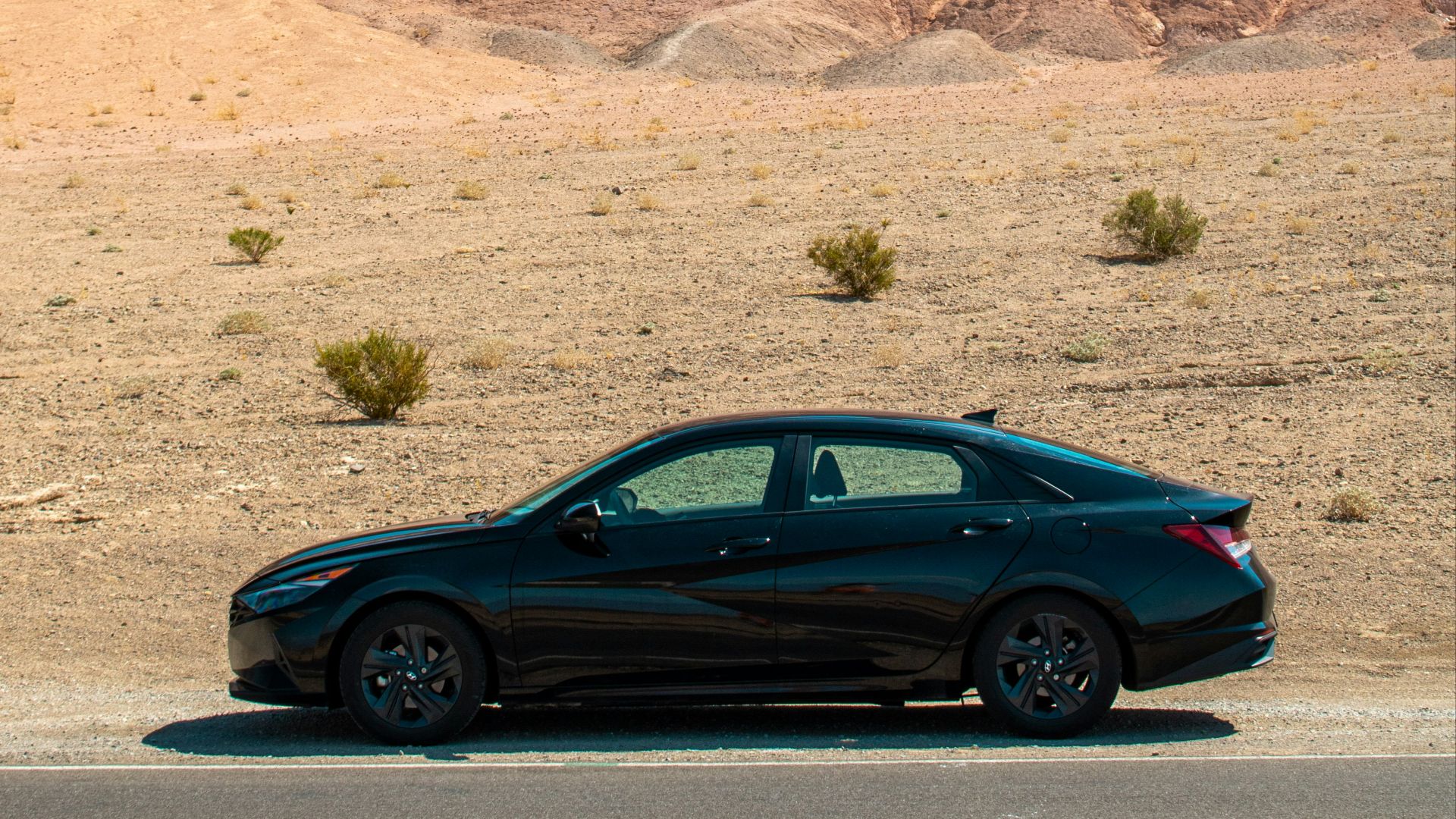 A black car driving down a desert road